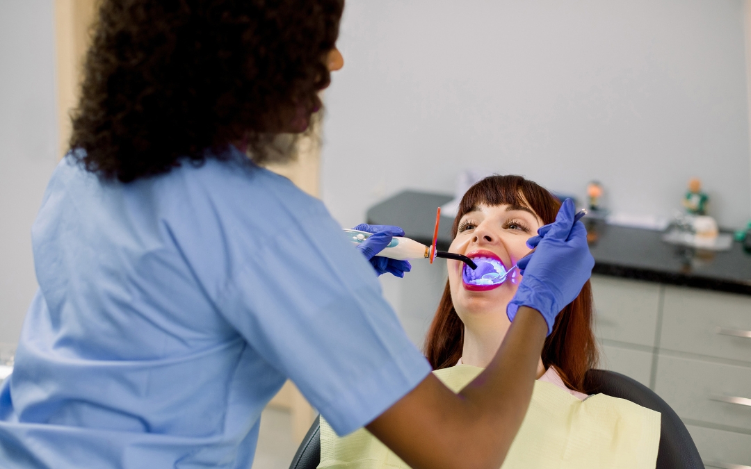 Dentist examining patient's teeth with UV light in modern dental clinic office.